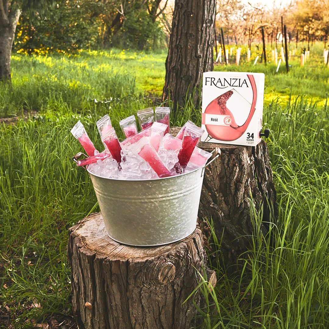 Franzia pink freezer pops in an ice bucket under a tree.