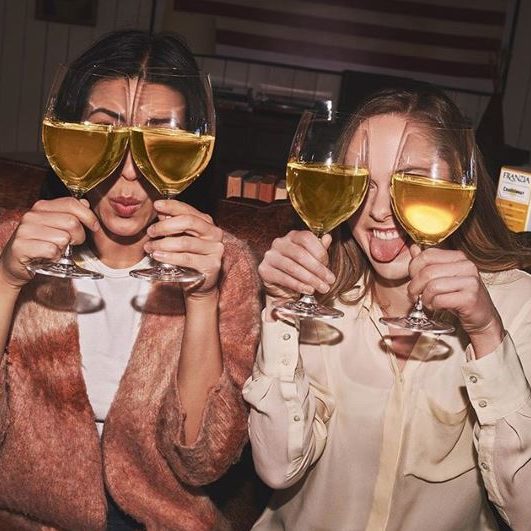 Two roommates holding up glasses of wine in front of their eyes for a silly picture