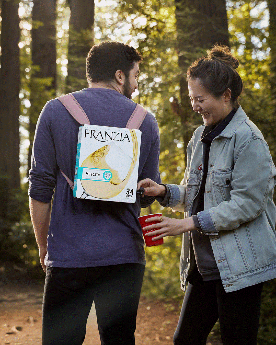 Two friends on a hike enjoying a glass of wine straight from a Franzia backpack