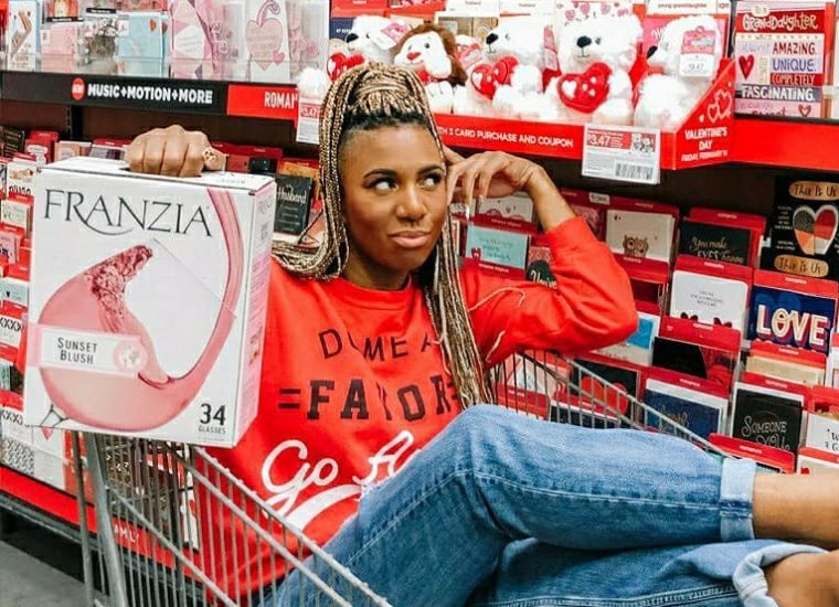 Woman sitting in a cart in front of a bunch of Valentine's Day cards with a box of Franzia Sunset Blush