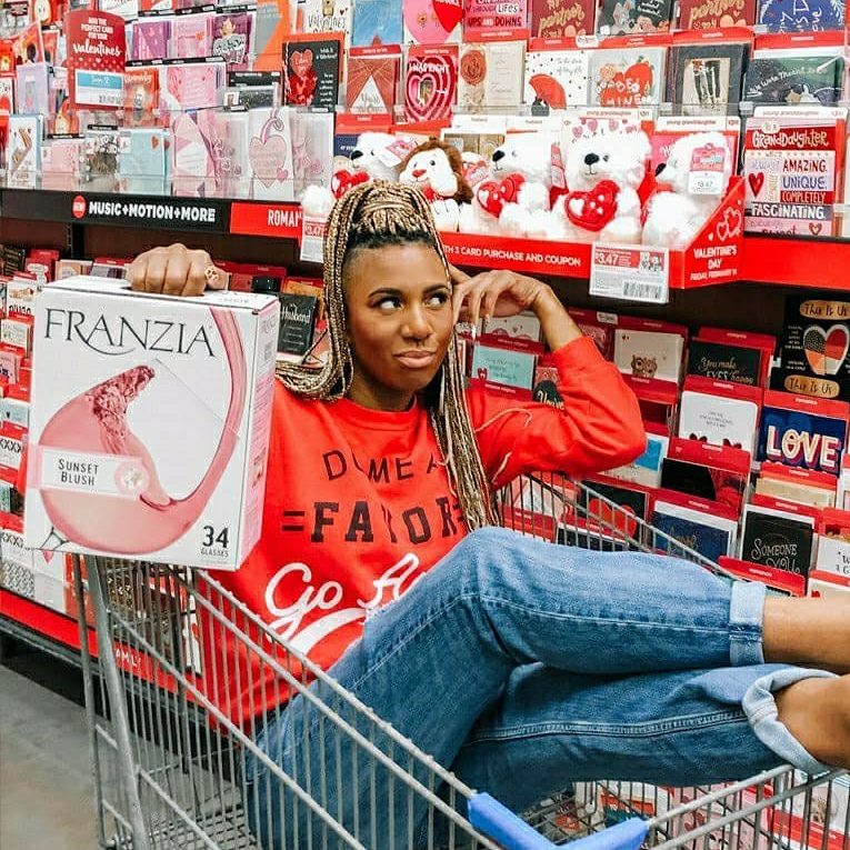 Woman sitting in a cart in front of a bunch of Valentine's Day cards with a box of Franzia Sunset Blush